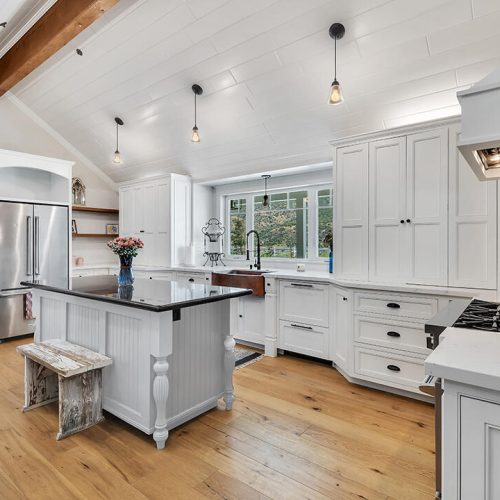 Contemporary white kitchen with island counter, hardwood floors, and pendant lighting.